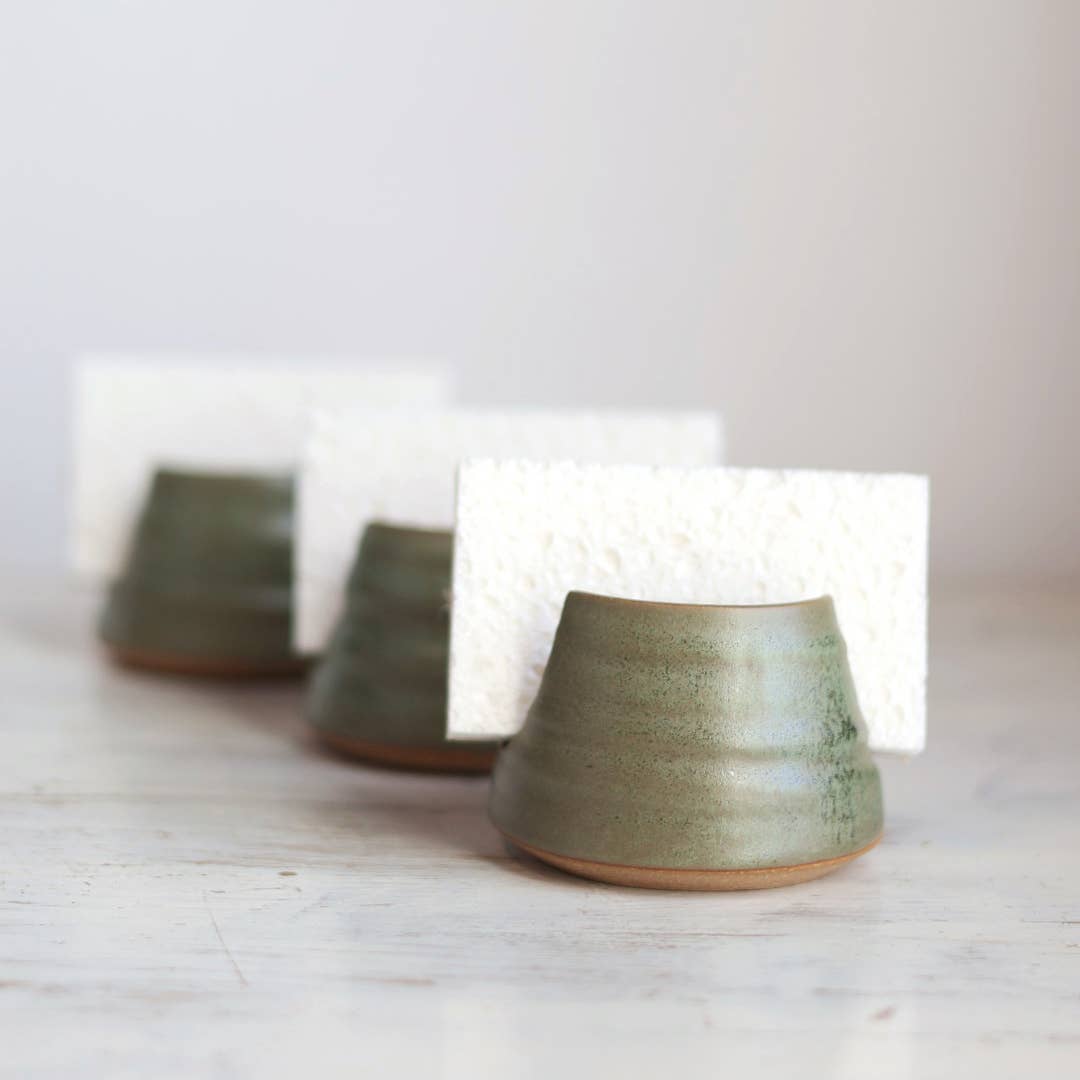 Three ceramic sponge holders on a light wooden surface with a white background