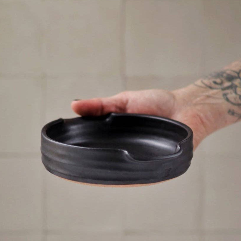 Person holding a black ceramic dish against a tiled wall background