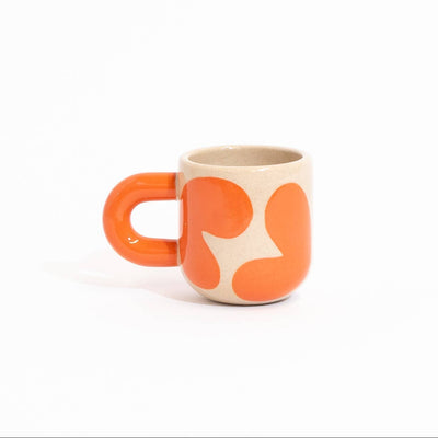 A small ceramic mug with a bright orange handle and body, decorated with an abstract pattern of orange shapes on a cream-colored base, set against a solid white background.