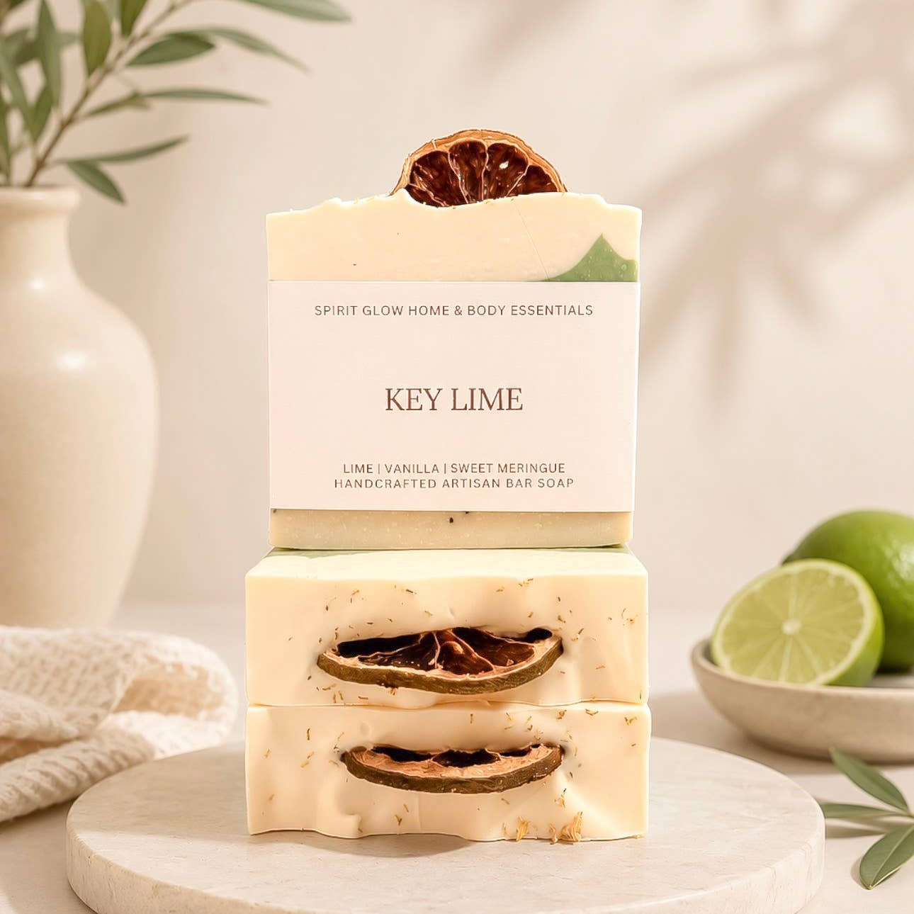 Three stacked bars of handmade artisan bar soap labeled 'KEY LIME' by Spirit Glow Home & Body Essentials, styled on a marble tray with limes and a vase in the background.