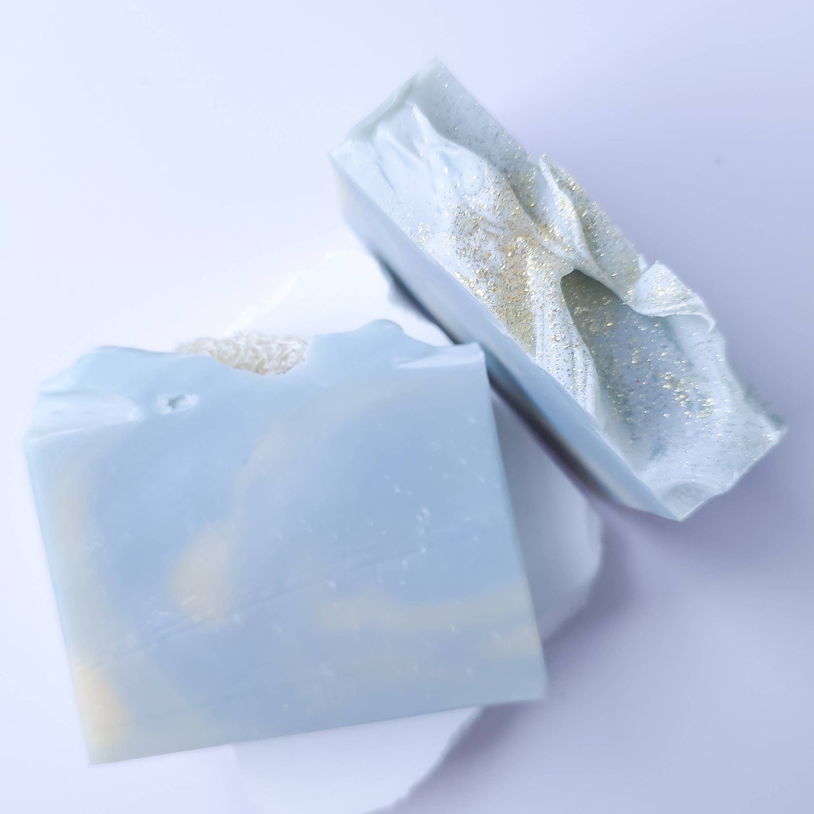 Two bars of soap with a gold leaf design on a light purple background