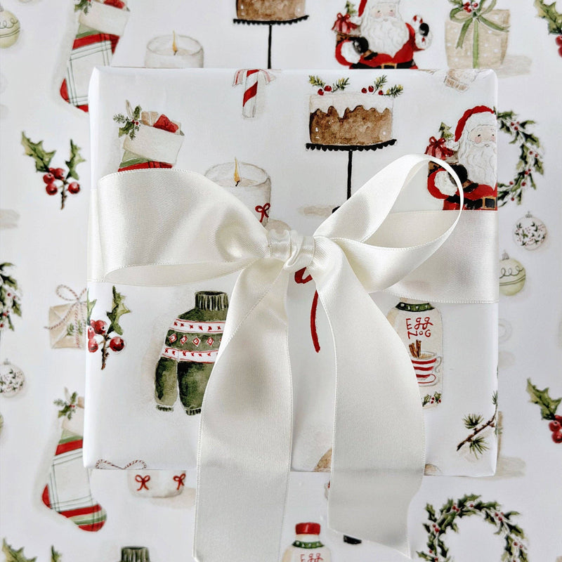 A roll of Christmas-themed wrapping paper with a festive watercolor print, shown alongside gold-handled scissors and a matching flat sheet of the paper on a white background.