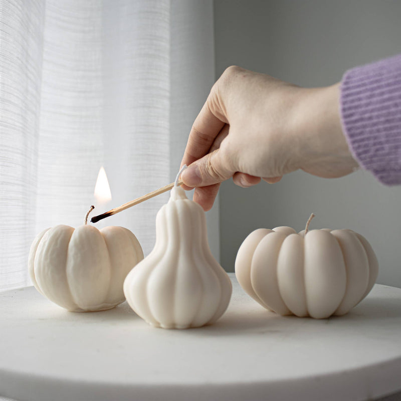 Three white pumpkin-shaped candles on a round surface with a neutral background