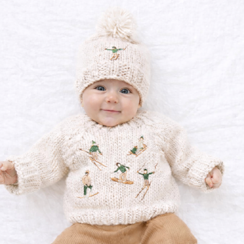 Knitted beanie with pom-pom and embroidered design on a white background
