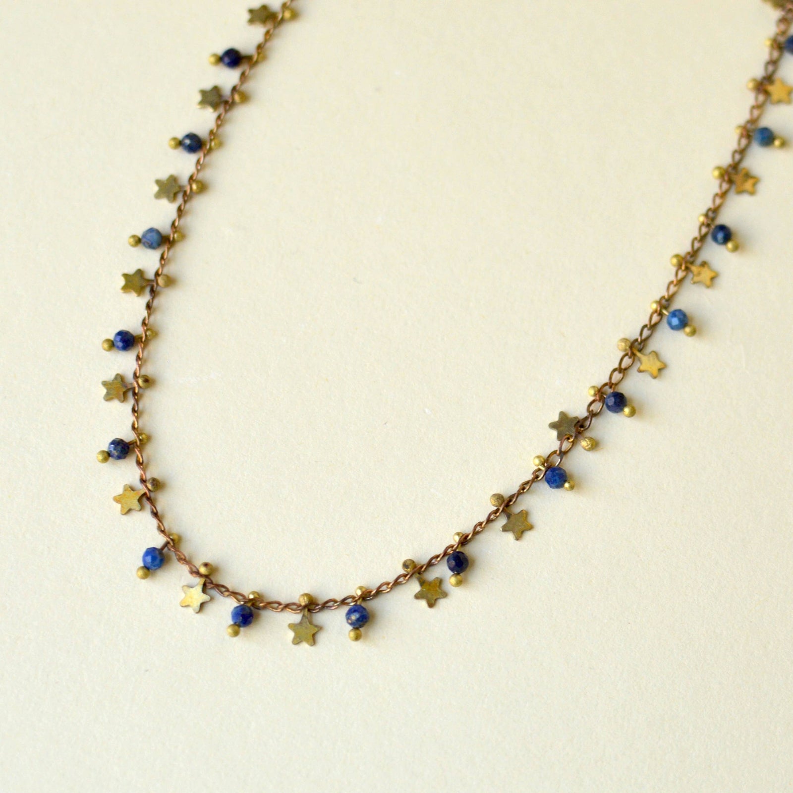 A necklace with tiny star and blue bead charms on a cream background.