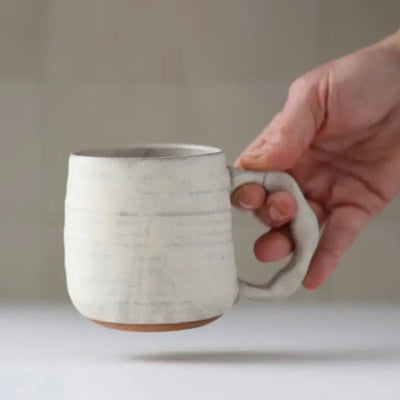 Hand holding a ceramic mug with a neutral background