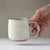 Hand holding a ceramic mug with a neutral background