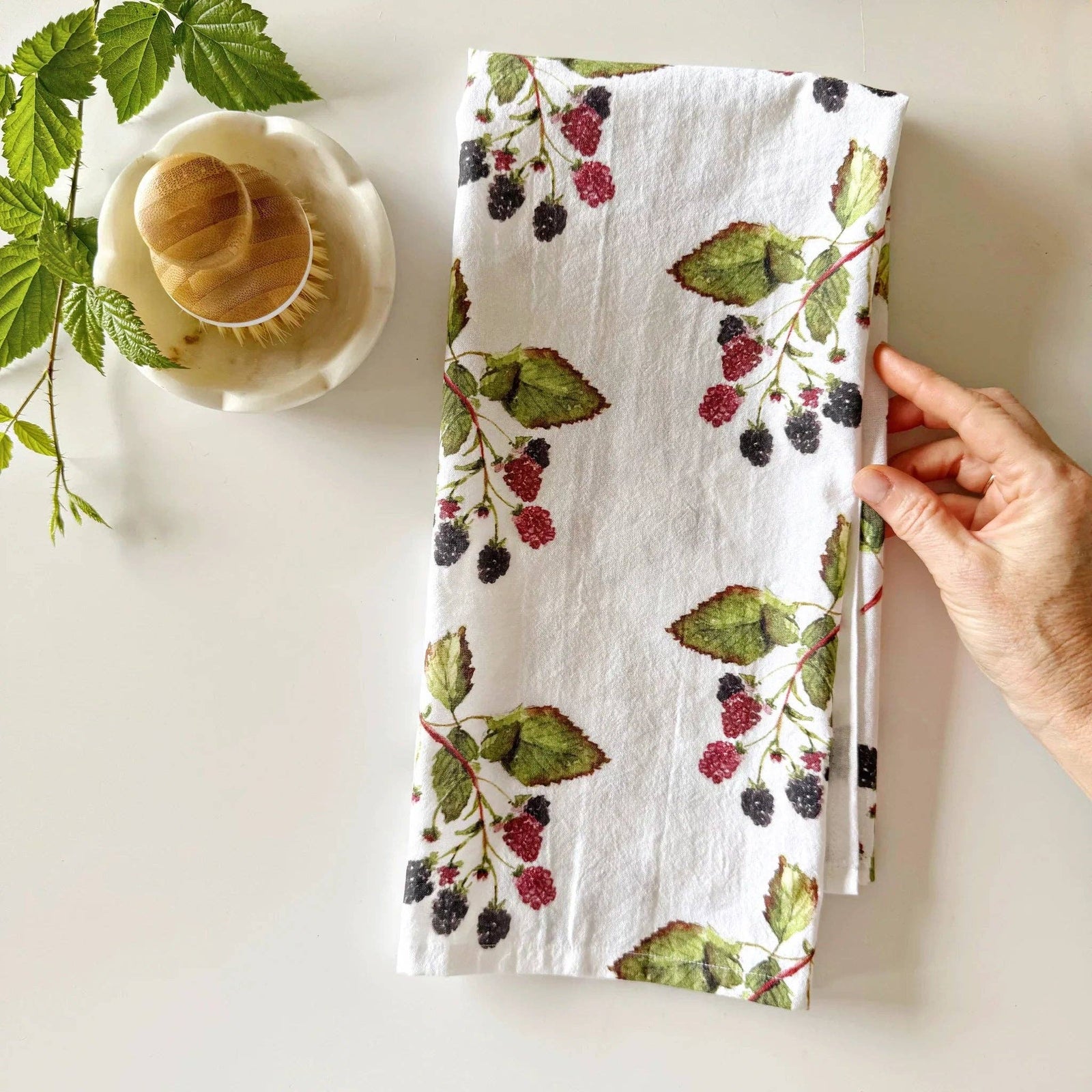 A hand holding a towel with a blackberry print on a light background 
