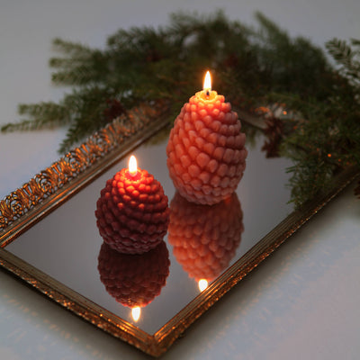Two textured candles with reflections on a mirror with greenery in the background