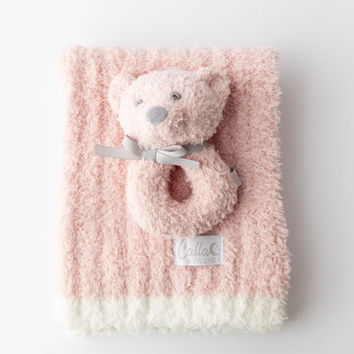 Pink fluffy blanket with a teddy bear rattle on a white background