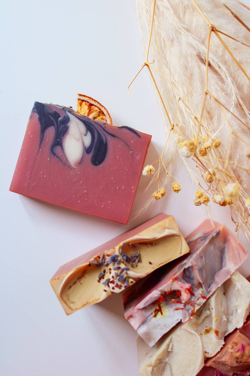 Three soap bars with natural designs on a wooden tray, surrounded by decorative elements including a pumpkin.