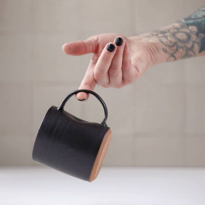 Person holding a black ceramic mug with a wooden handle against a neutral background