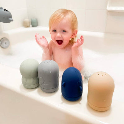 Child in a bathtub with four colorful bath toys on the edge.