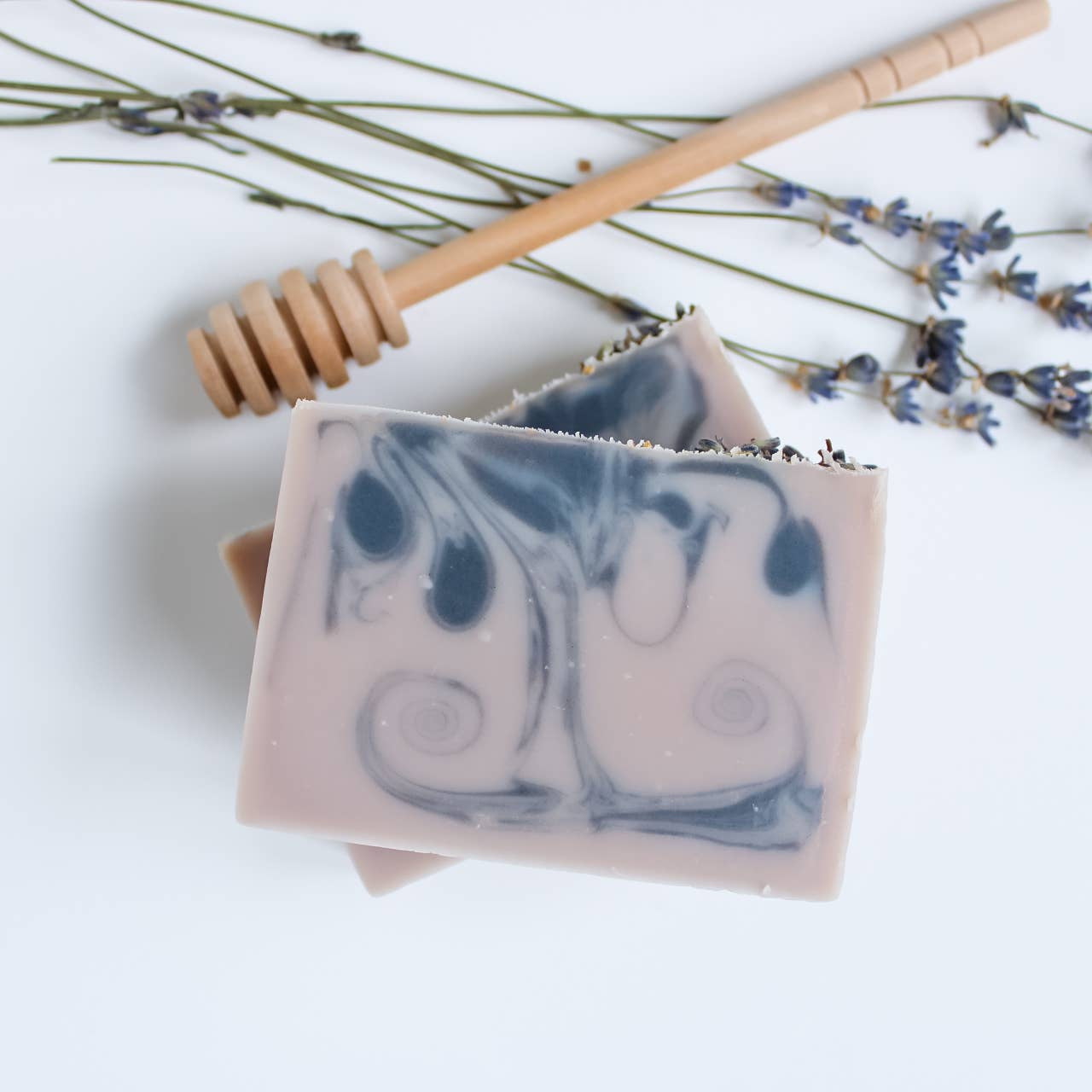 Two soap bars with a blue design on a white background with lavender flowers and a honey dipper.