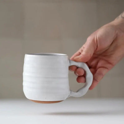 Hand holding a white ceramic mug against a neutral background