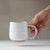 Hand holding a white ceramic mug against a neutral background