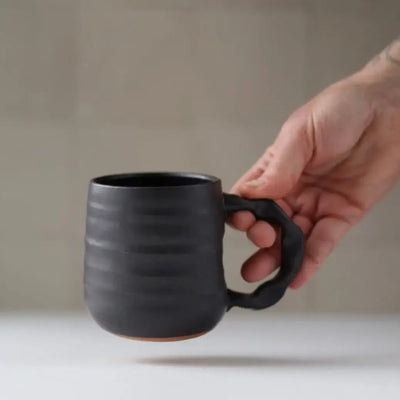 Hand holding a black ceramic mug against a neutral background