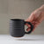 Hand holding a black ceramic mug against a neutral background