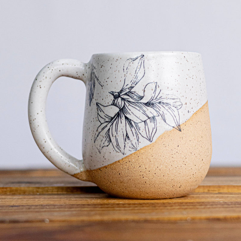 Ceramic mug with leaf design on a white surface, Christmas tree in the background
