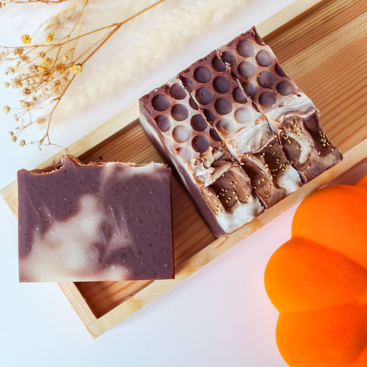 Two soap bars on a wooden board with a pumpkin and dried flowers in the background