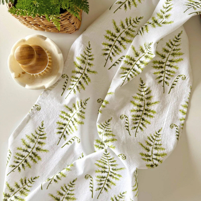 A hand holding a towel with a fern print on a light background