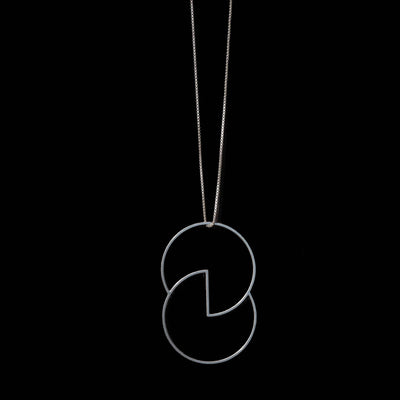 A silver-toned necklace featuring a minimalist, interlocking circular pendant on a fine chain, set against a solid black background.