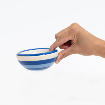 A hand holding a small ceramic bowl with blue and white horizontal stripes against a solid white background.