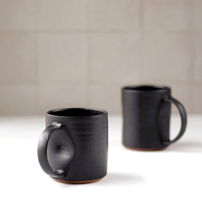 Two black ceramic mugs on a light surface with a neutral background