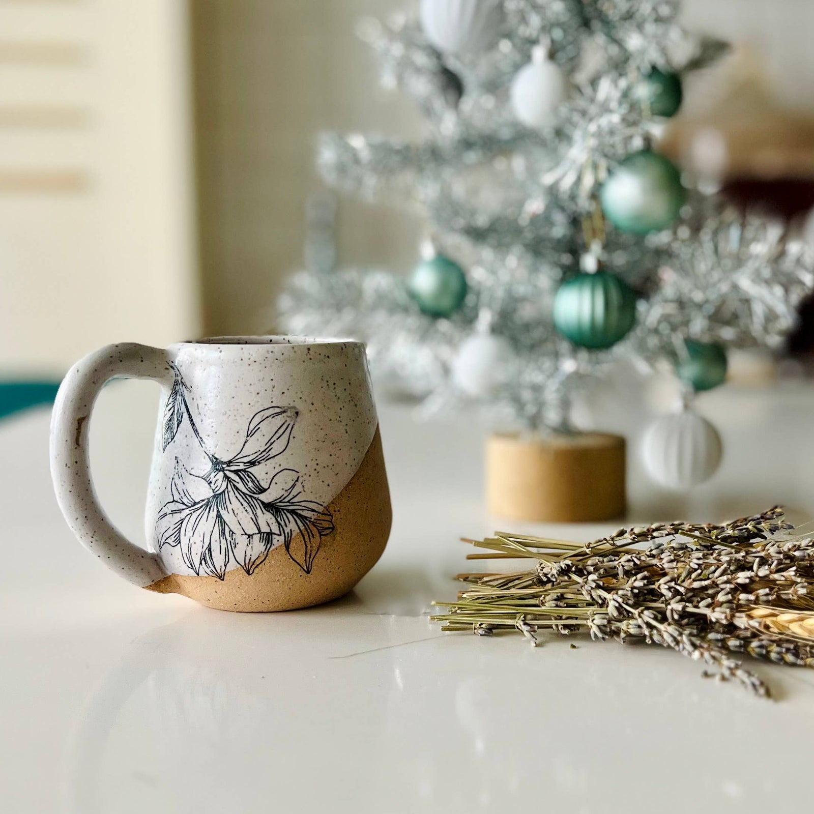 Ceramic mug with leaf design on a white surface, Christmas tree in the background