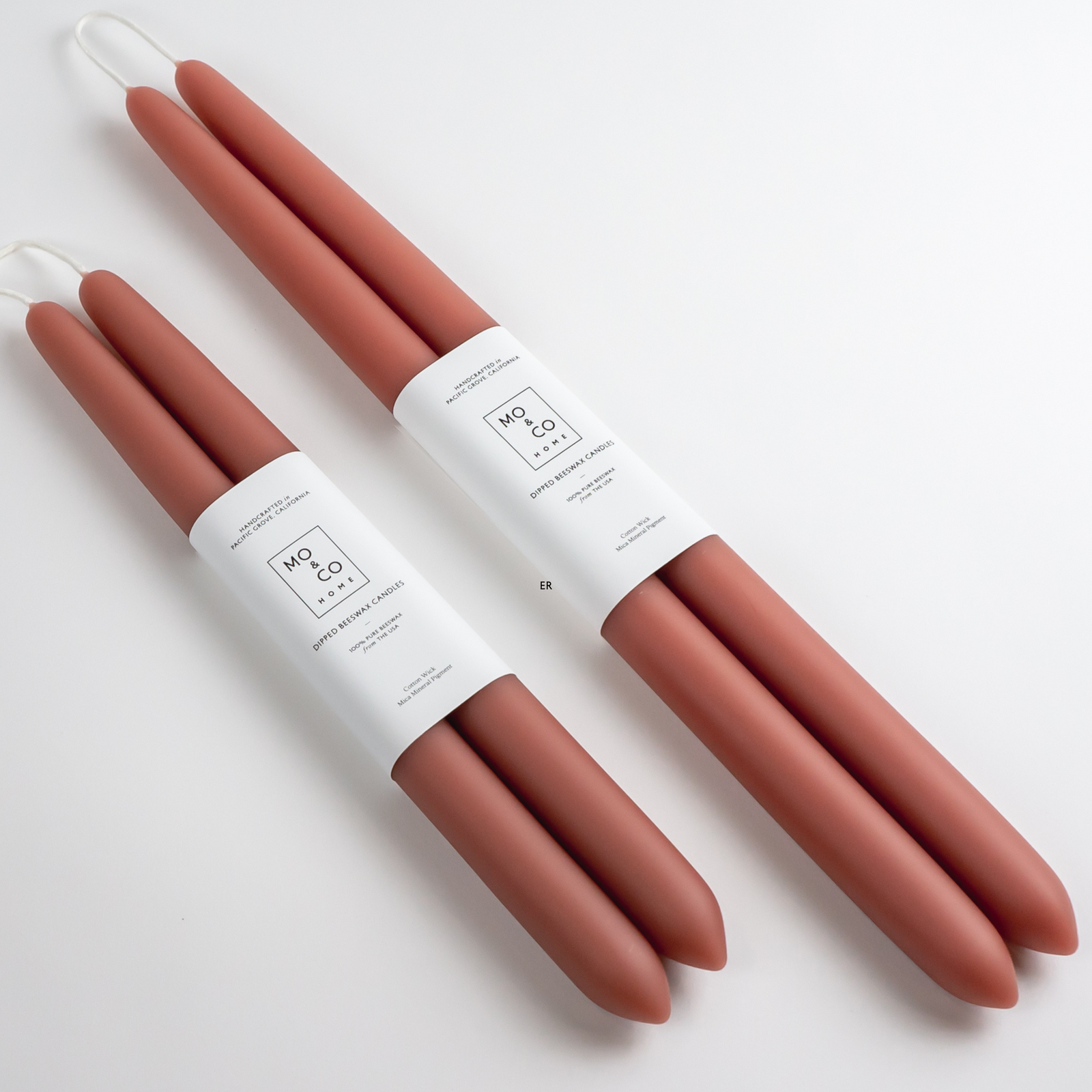 Set of four terracotta-colored candles with white labels on a white background