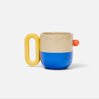 A ceramic mug with a split beige and blue body, a yellow handle, and a small orange protruding accent, shown on a white background.