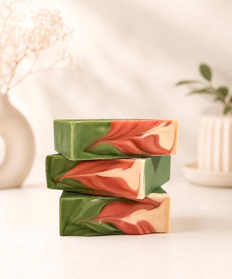 Two stacked handmade artisan bar soaps labeled 'BAJA CACTUS' by Spirit Glow Honey & Body Essentials, featuring green, coral pink, and cream swirls, set against a soft, warm, blurred background with a white vase and towel.