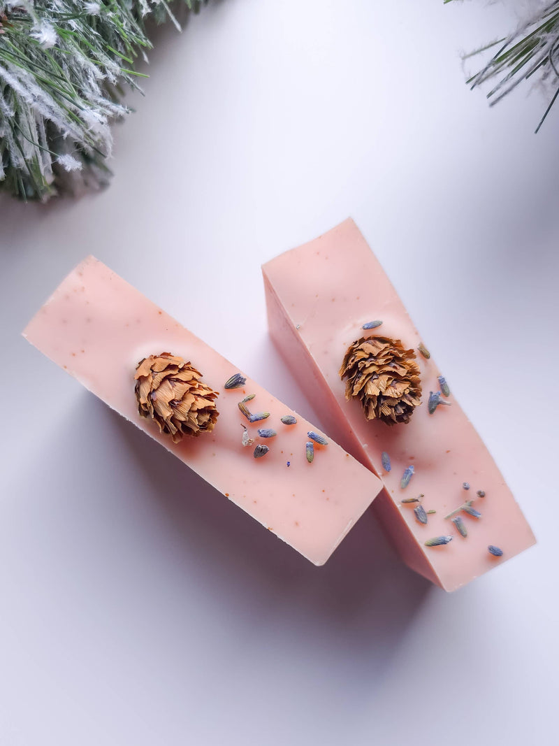 Two pink soap bars with decorative elements on a white surface with snow and pine branches.