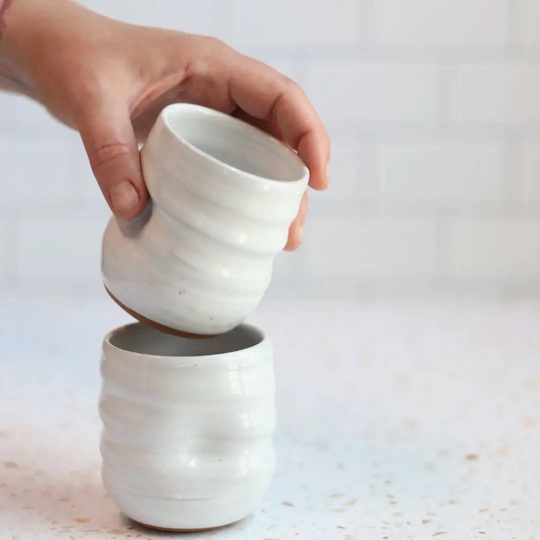 Hand holding a white ceramic cup over another similar cup on a light background