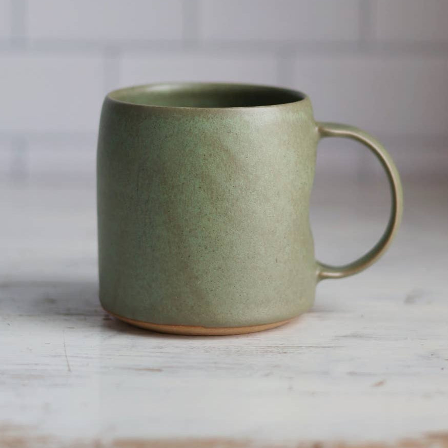 Green ceramic mug on a marble surface with a tiled wall background