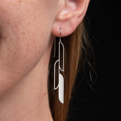 A close up of a woman wearing silver earrings on a black background