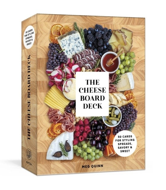 The Cheese Board Deck card game box by Meg Quinn, featuring a rustic wooden board design filled with cheeses, grapes, cured meats, crackers, and citrus slices. The front displays the title 'THE CHEESE BOARD DECK' 