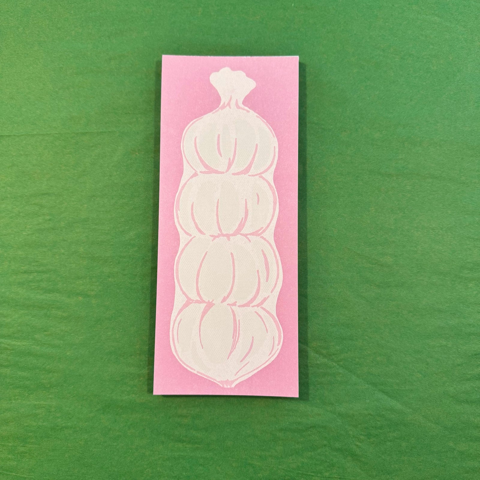A pink notepad with an illustration of garlic on a green background