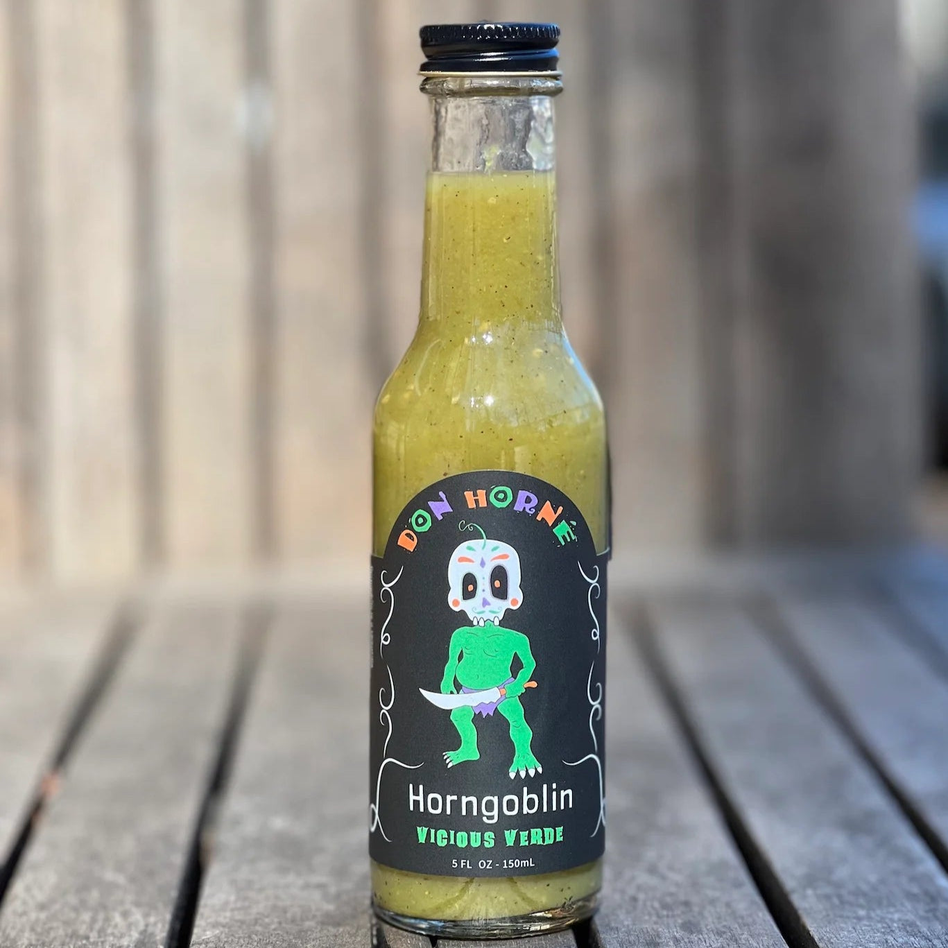 Bottle of Don Horne's Horngoblin Vicious Vindication hot sauce on a wooden surface with a blurred background.