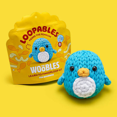 A blue and white penguin toy sits in front of its bright yellow retail packaging on a solid yellow background.
