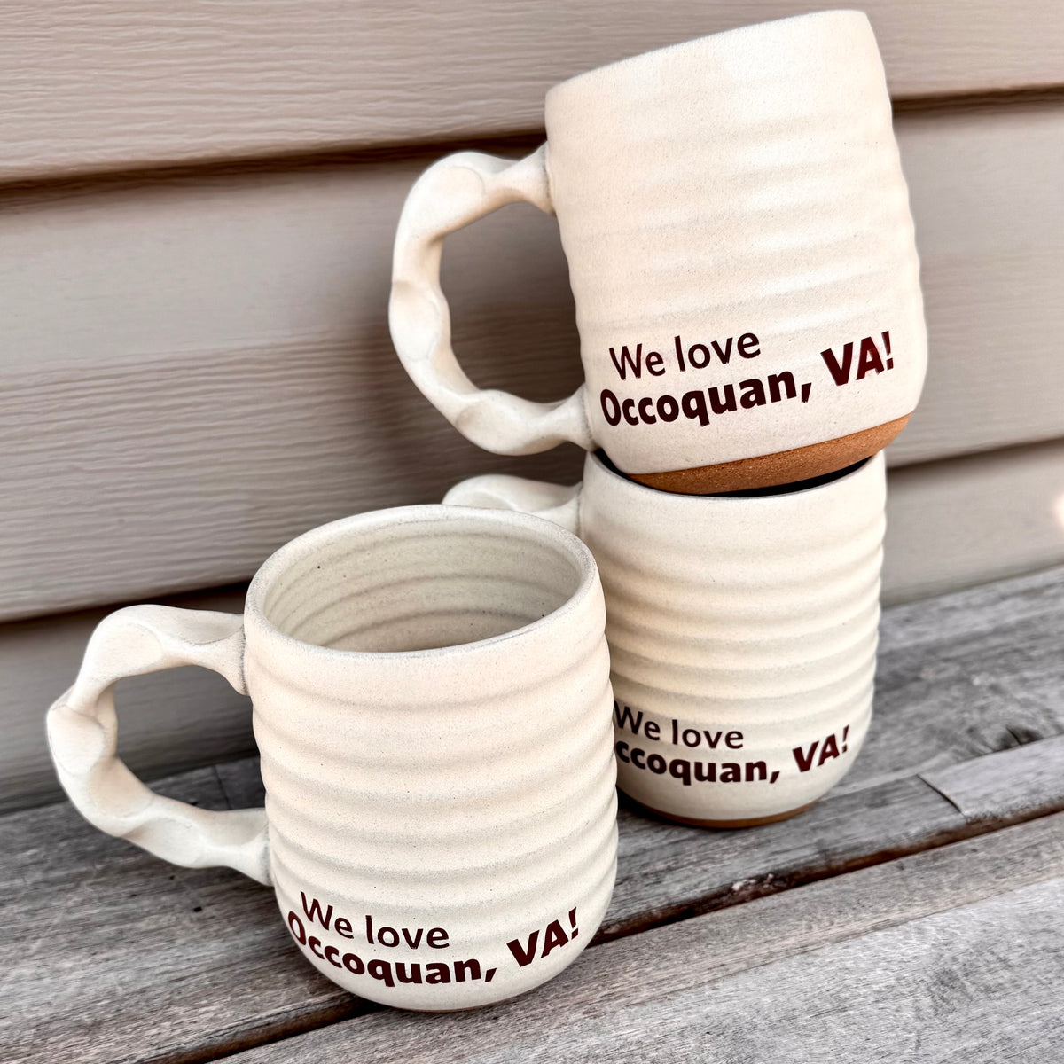 Two ceramic mugs with 'We love Occoquan, VA!' text on a wooden surface.
