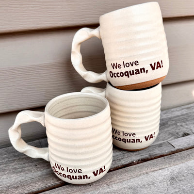 Two ceramic mugs with 'We love Occoquan, VA!' text on a wooden surface.