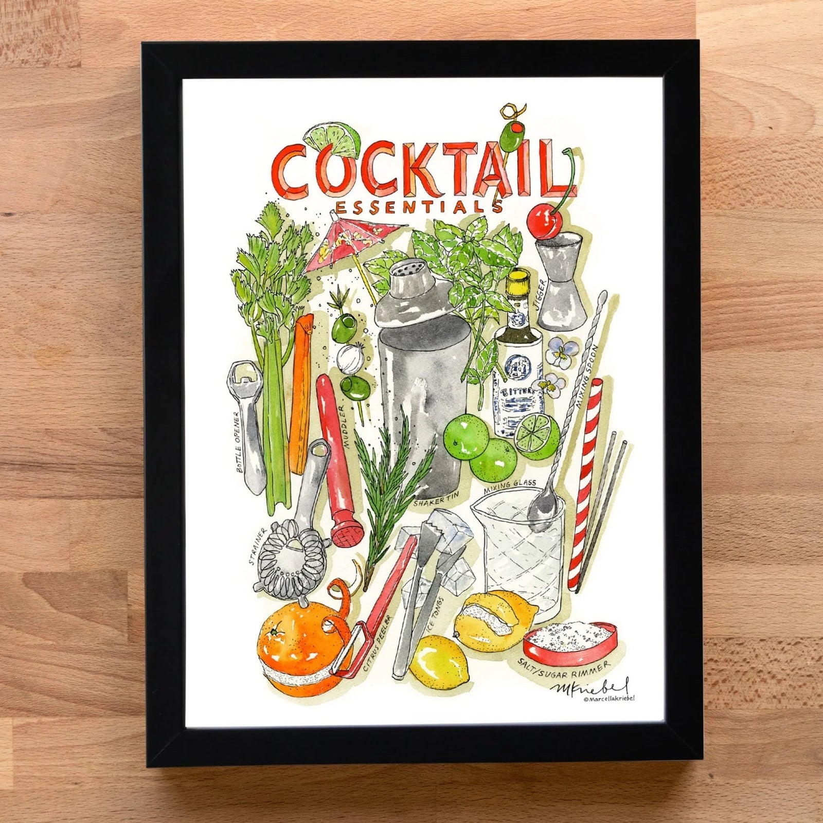 A framed art print titled 'Cocktail Essentials' featuring a colorful watercolor illustration of cocktail ingredients and tools, displayed on a light wood background.