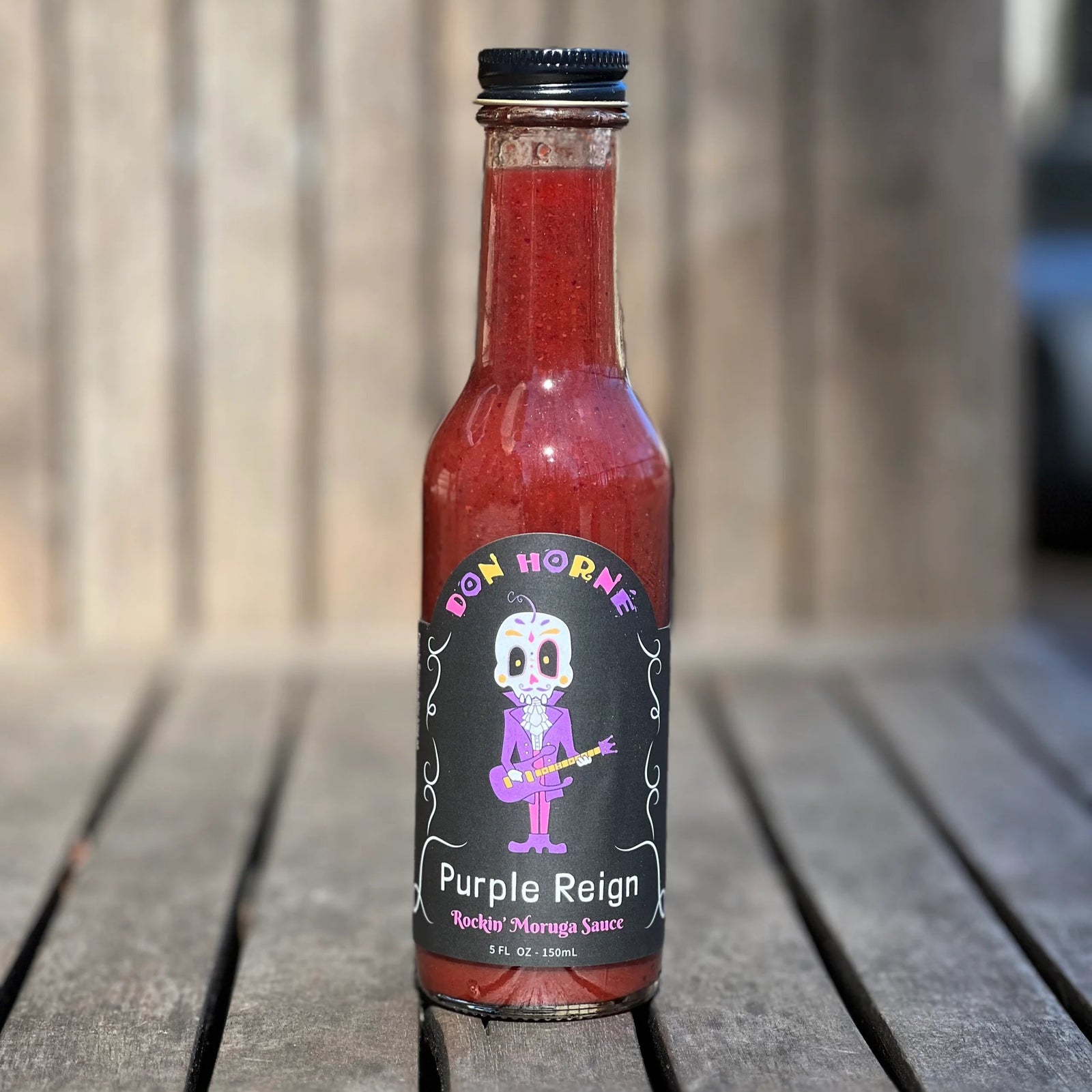 Bottle of Don Horne Purple Reign hot sauce on a wooden surface with a blurred background
