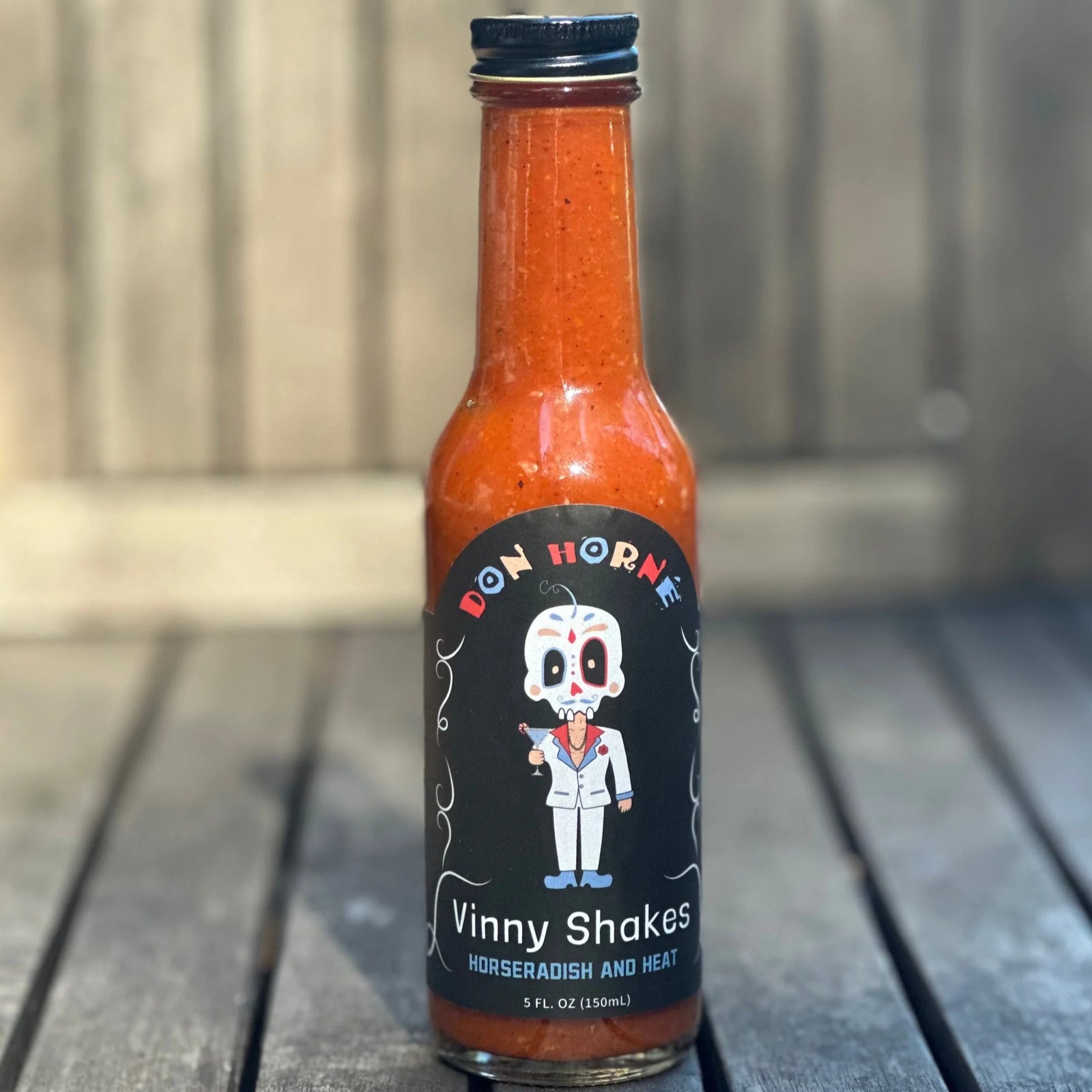 Bottle of Bon Horne Vinny Shakes hot sauce on a wooden surface with a blurred background