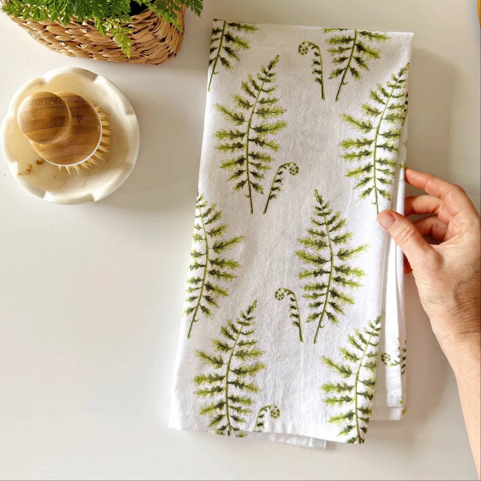 A hand holding a towel with a fern print on a light background