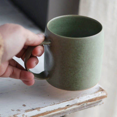 Hand holding a green ceramic mug on a wooden surface