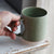 Hand holding a green ceramic mug on a wooden surface
