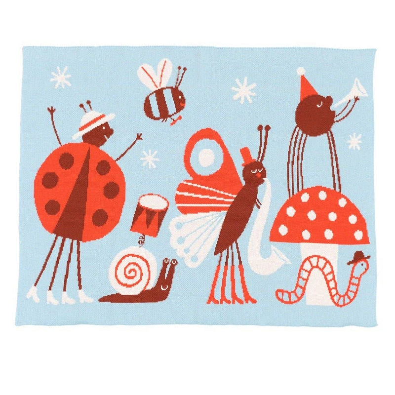 A light blue fabric blanket or throw featuring whimsical cartoon bugs and mushrooms, held up by a person's hands on a wooden stand against a white background.
