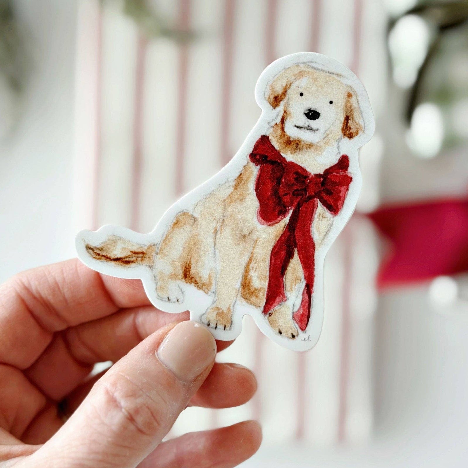A hand holding a sticker of a dog with a red bow on a light blurry background